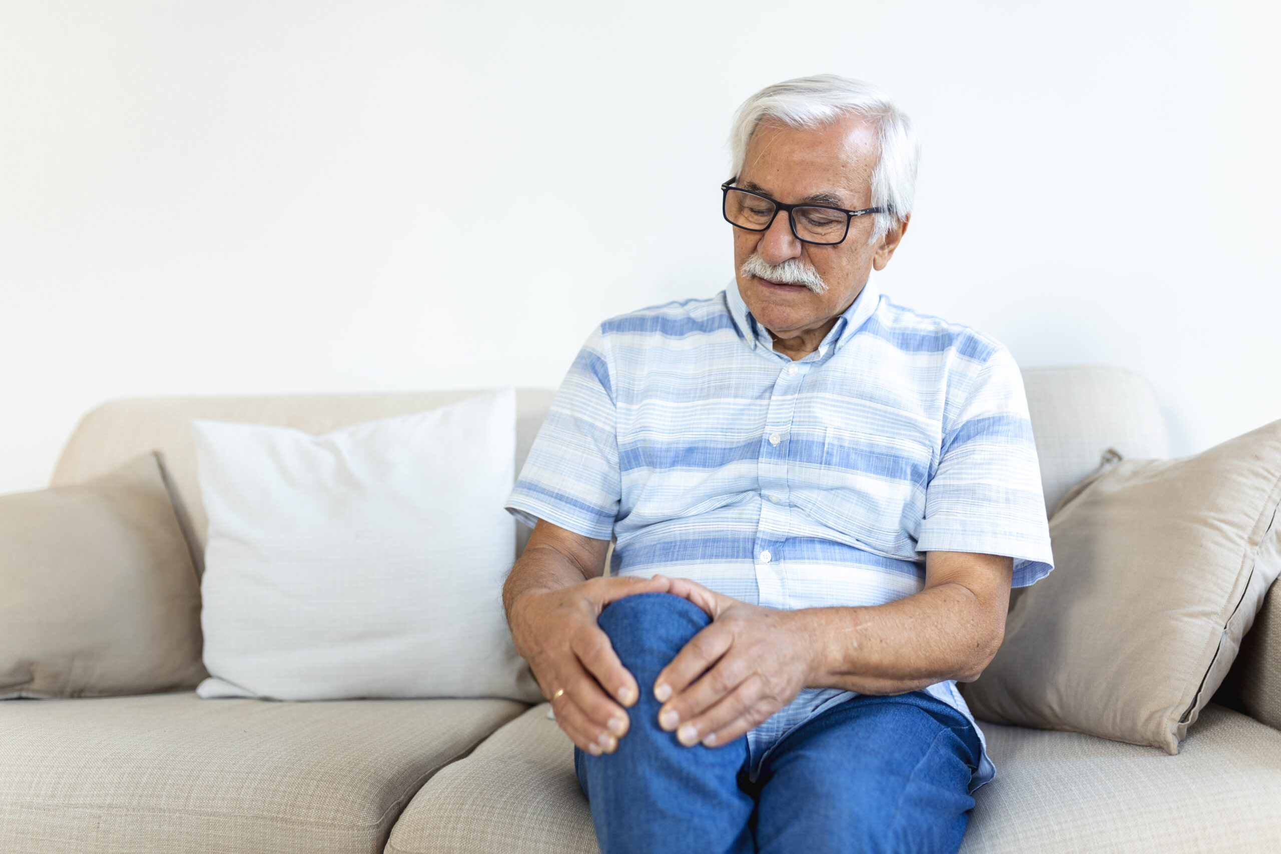 elderly-man-sitting-sofa-home-touching-his-painful-knee-people-health-care-problem-concept-unhappy-senior-man-suffering-from-knee-ache-home-scaled